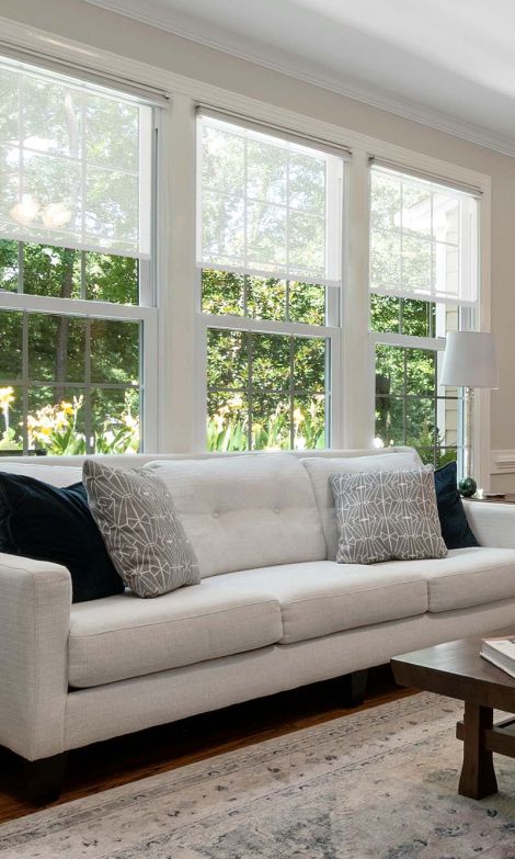 a white couch in front of three windows with shades on them