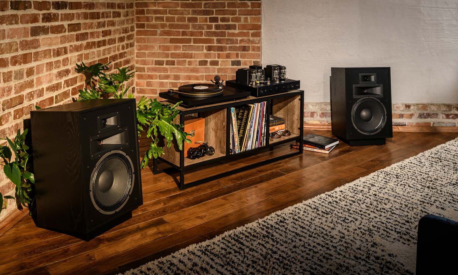 klipsch speakers sitting on the floor in a room with brick walls and wooden floors